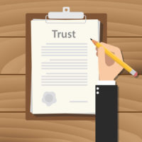 trust concept agreement with hand hold pencil signing paper document on clipboard on wood table