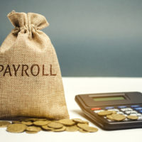 Money bag with the word Payroll and calculator. Payroll is the sum total of all compensation a business must pay to its employees for a set period of time or on a given date. Taxes. Management