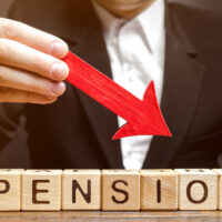 A man holds an arrow down over wooden blocks with the word Pension. Fall / reduction pension payments. Retirement. Financing retirees. Reduction of the pension fund. The low size of pensions.